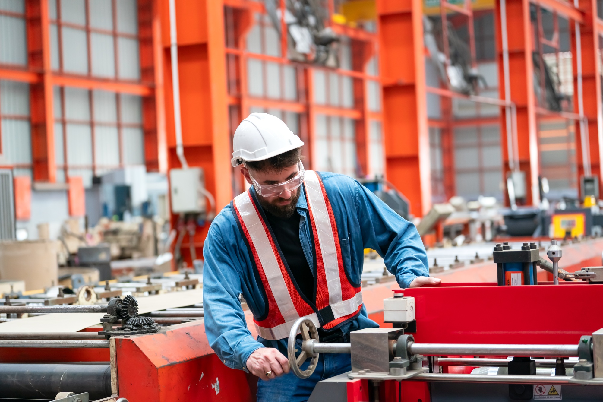 Inside a factory, industrial worker in action on metal press machine holding a piece of steel